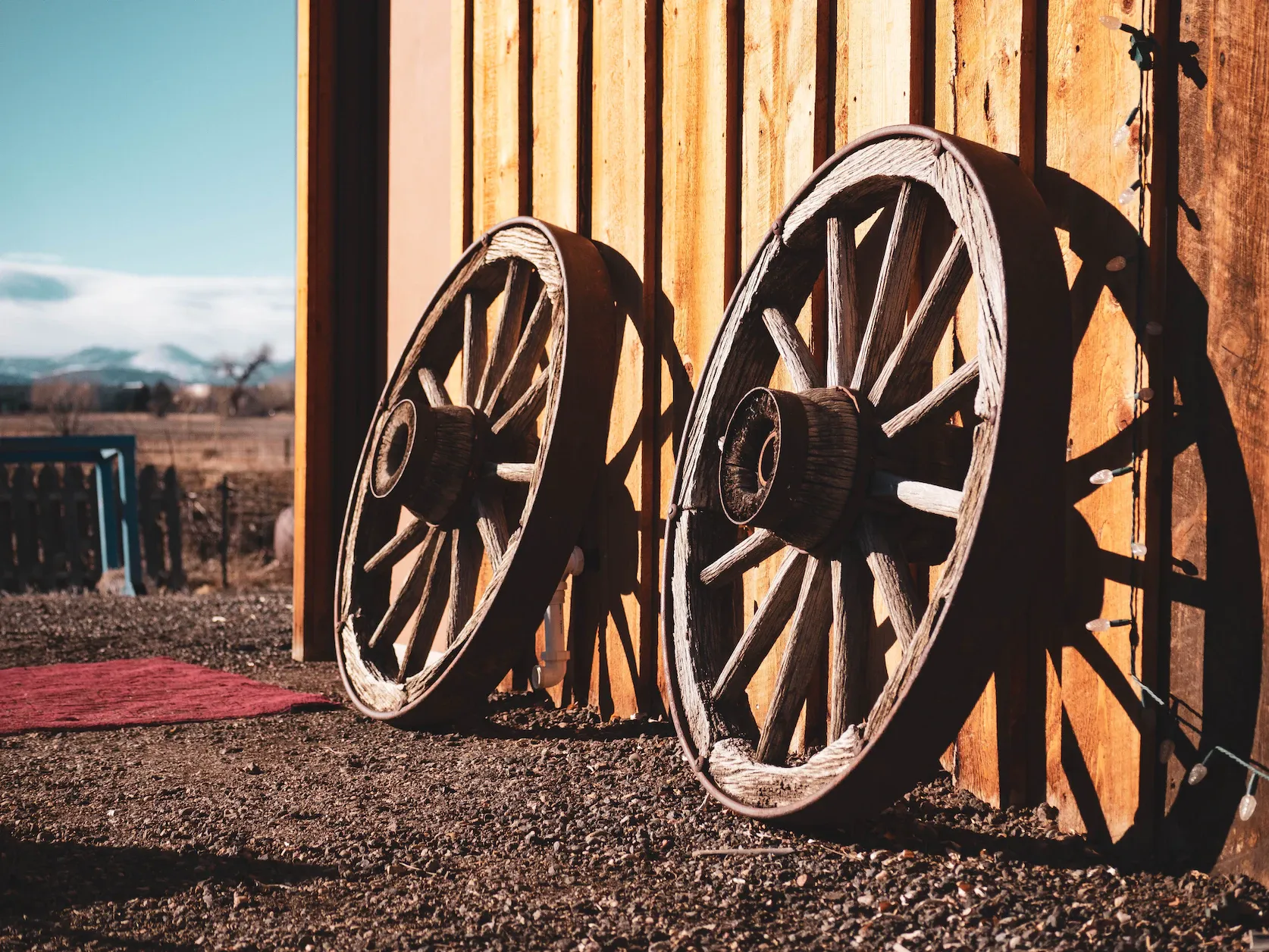 Two old carriage wheels leaning against a wall outside.