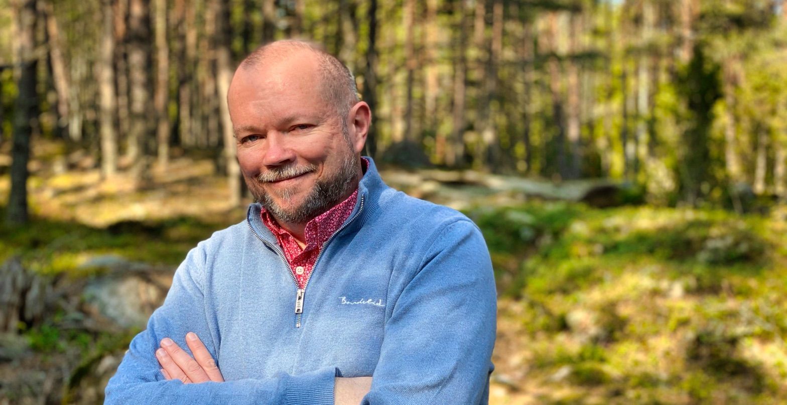Per Axbom standing with arms crossed - smiling at the camera - with greenery and forest in the background.