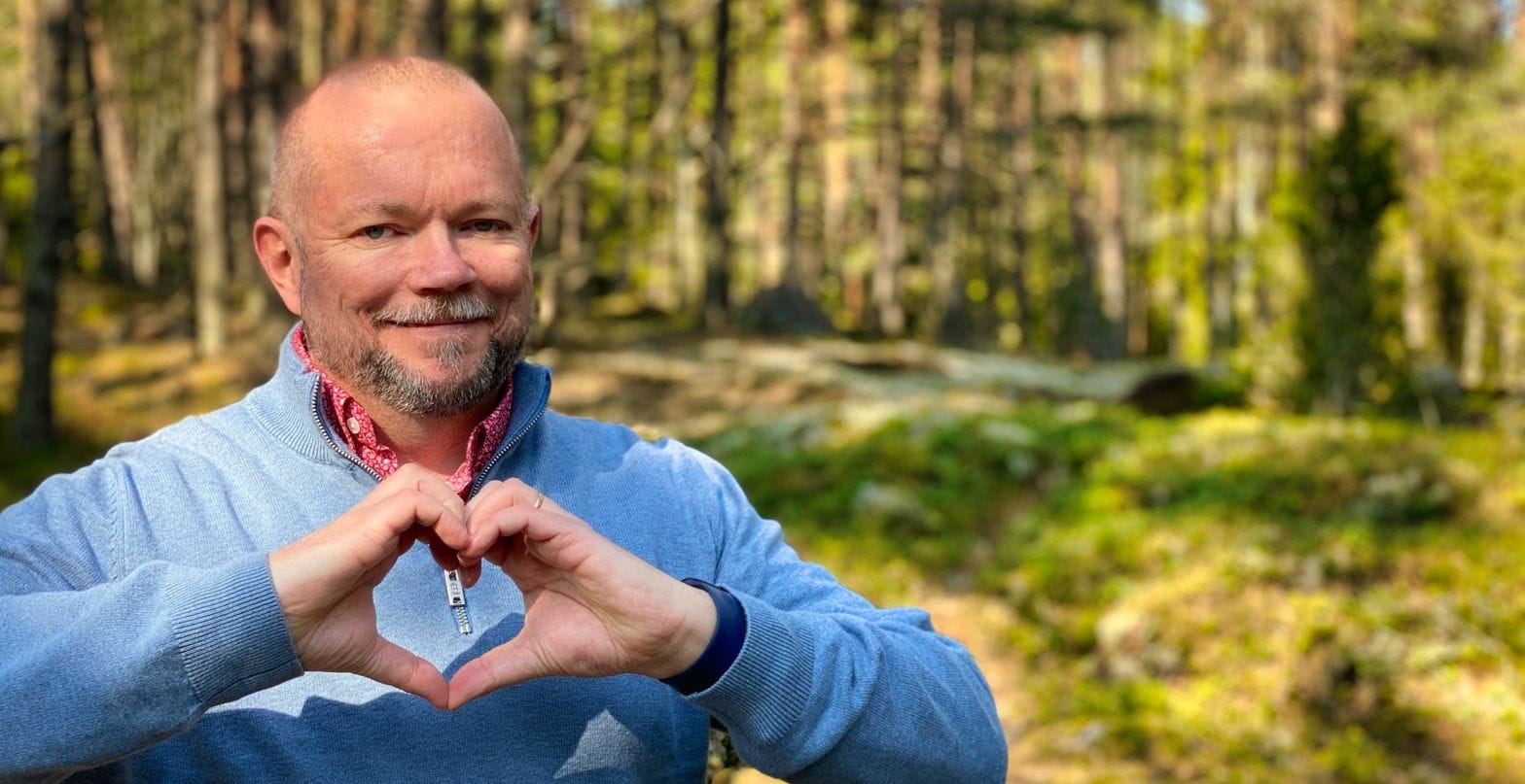 Per Axbom holding his hands in a heart symbol, with the forest as a background.