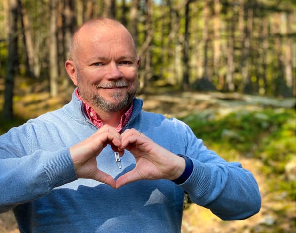 Per Axbom smiling, against a forest backdrop, and holding up his hands to form a heart shape.