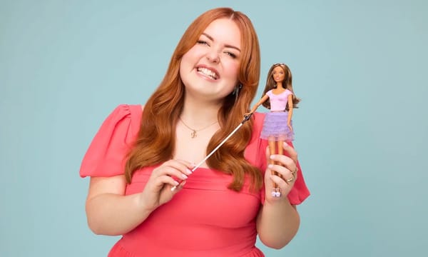 A smiling Lucy Edwards holds up the new Barbie doll with a white cane