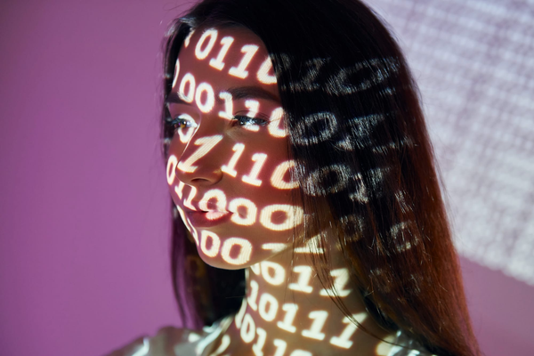 Close-up headshot of a woman with binary numbers, ones and zeroes, projected across her face.